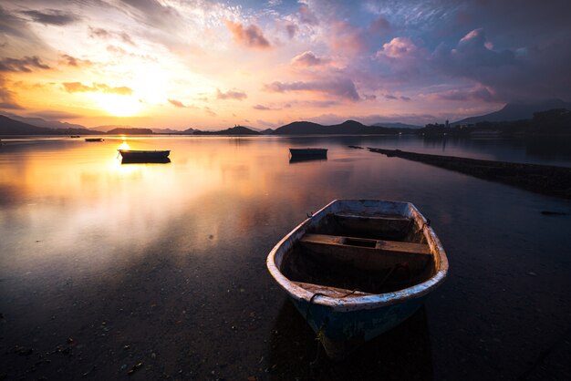 Bela foto de um pequeno lago com um barco a remo de madeira em foco e nuvens surpreendentes no céu