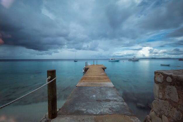 Bela foto de um píer que leva ao oceano sob o céu sombrio em Bonaire, Caribe