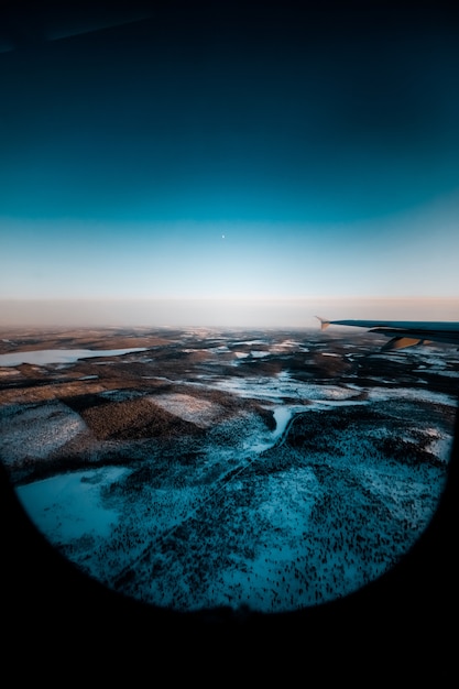 Bela foto de uma asa de avião pela janela sobre uma paisagem coberta de neve