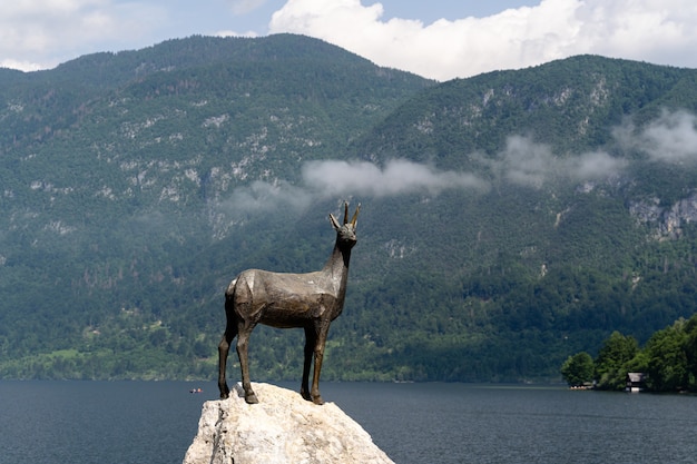 Bela foto de uma estátua de Goldhorn no Lago Bohinj cercada por montanhas e árvores
