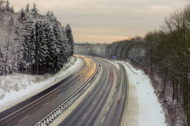 Bela foto de uma estrada com árvores na floresta coberta de neve durante o inverno