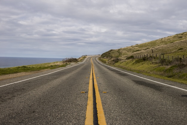 Bela foto de uma estrada de asfalto cercada por montanhas e o oceano em um dia nublado