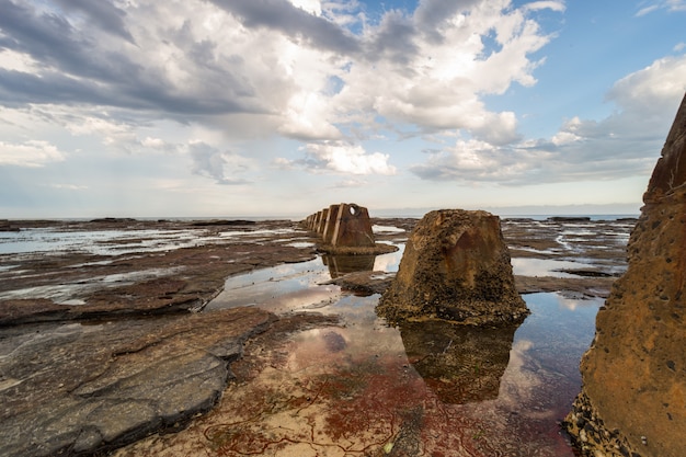 Bela foto de uma formação rochosa marrom, rodeada pela água do oceano sob o céu nublado