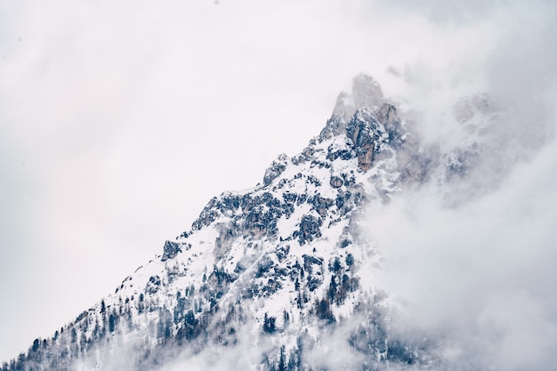 Bela foto de uma montanha nublada coberta de neve com céu cinza