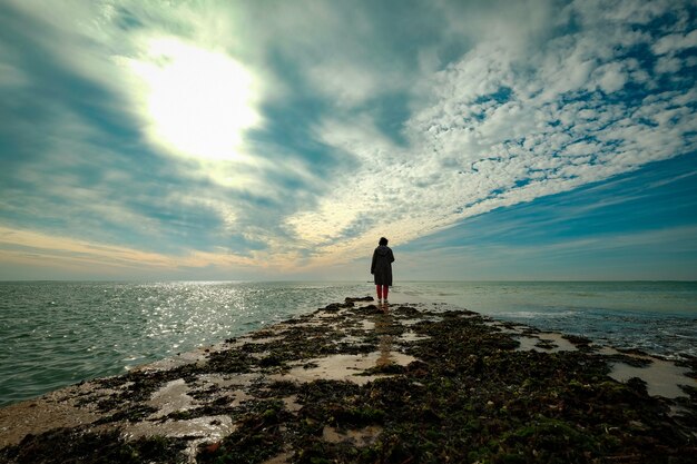 Bela foto de uma pessoa caminhando em um terreno dentro do oceano sob um céu nublado