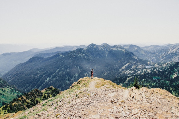 Bela foto de uma pessoa em pé na beira do penhasco com montanhas arborizadas