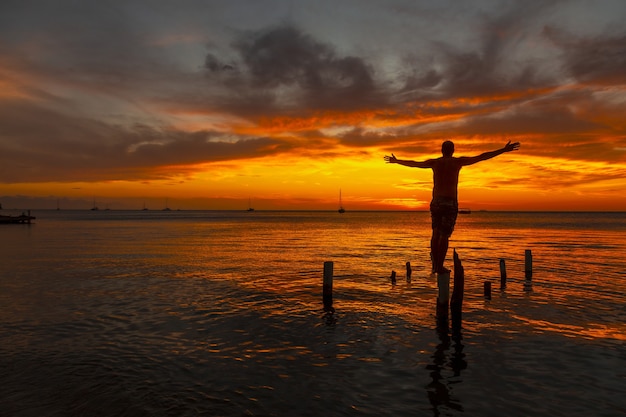 Bela foto de uma silhueta masculina de pé sobre palafitas de madeira na água