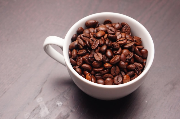 Bela foto de xícara branca cheia de grãos de café em uma mesa de madeira