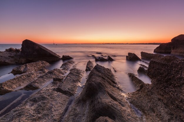 Bela foto do mar com falésias e pedras durante o pôr do sol