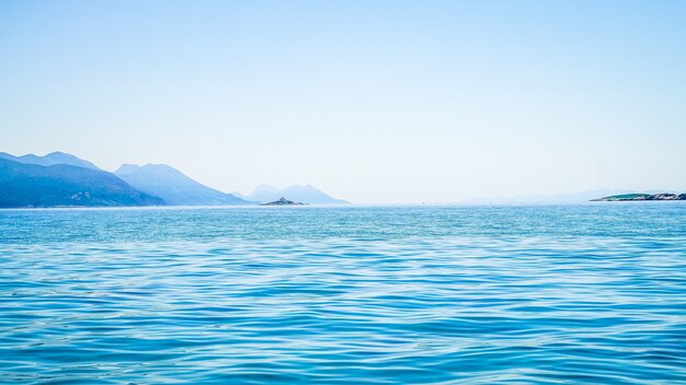 Bela foto do mar com uma montanha à distância e um céu claro