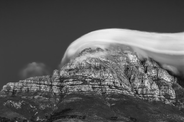 Bela foto em escala de cinza de um penhasco rochoso coberto por nuvens de tirar o fôlego