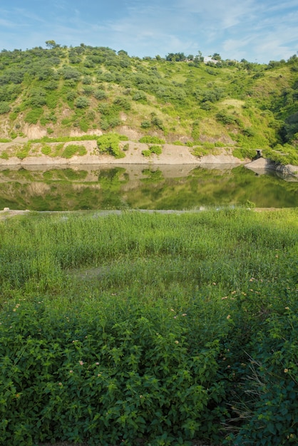 Bela foto vertical de um campo verde e um lago com uma colina