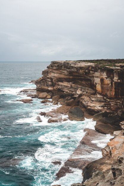 Bela foto vertical de um grande penhasco próximo à água azul em um dia sombrio