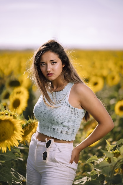 Bela foto vertical de uma jovem mulher posando em um campo de girassóis brilhantes em um dia ensolarado