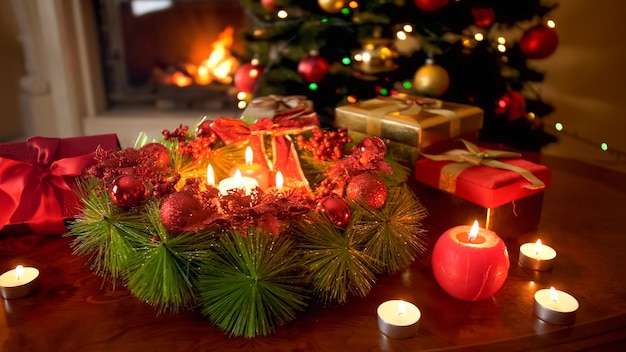 Bela imagem de mesa decorada com grinalda e velas contra a árvore de natal e fogo aceso na lareira