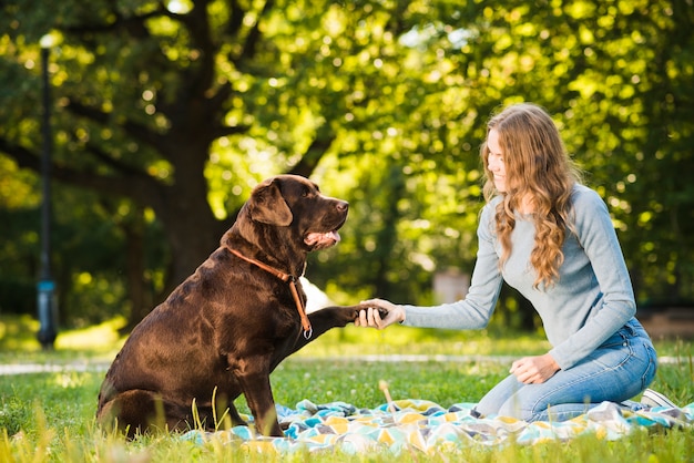 Bela jovem agitando a pata do cão no jardim