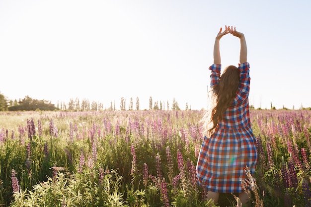 Foto grátis bela jovem andando no campo de flores durante o pôr do sol, usar vestido de luz de verão.