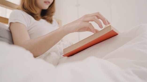 Bela jovem asiática atraente lendo um livro enquanto estava deitado na cama