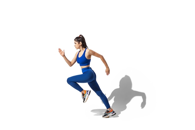 Bela jovem atleta praticando no fundo branco do estúdio, retrato com sombras. Modelo de ajuste esportivo em movimento e ação.