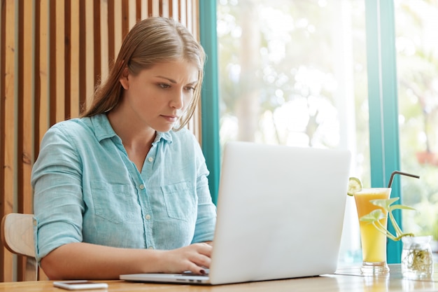 Bela jovem com cabelo comprido sentada num café com um laptop