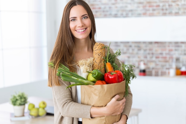 Bela jovem com legumes em saco de compras em casa.