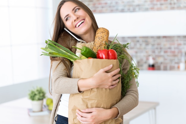 Bela jovem com legumes em saco de compras em casa.