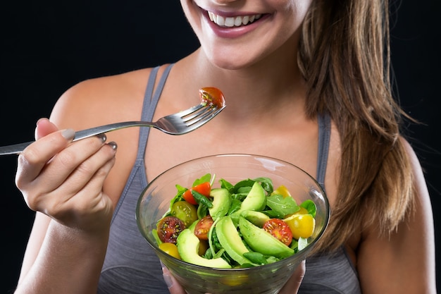 Bela jovem comendo salada sobre fundo preto.