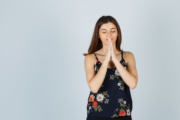 Foto grátis bela jovem de mãos dadas em um gesto de oração na blusa e parecendo esperançosa