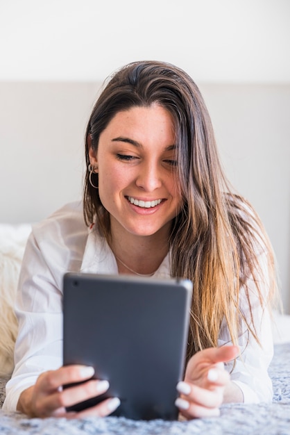 Bela jovem deitada na cama, olhando para tablet digital