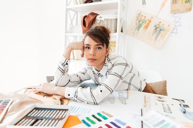 Bela jovem designer de moda feminina, sentado em sua mesa de trabalho