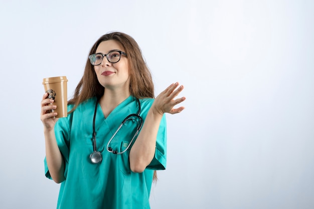 Bela jovem enfermeira com estetoscópio segurando uma xícara de café