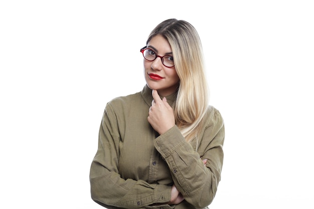 Bela jovem estilista talentosa com cabelo loiro em pé isolado em um quarto branco, segurando o dedo no queixo, pensando no conceito de sua nova coleção de joias, tendo um sorriso alegre e satisfeito