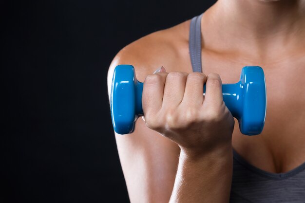 Bela jovem levantando dumbbells sobre fundo preto.