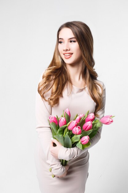 Bela jovem loira com um buquê de tulipas cor de rosa isoladas na parede branca.