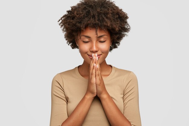 Bela jovem negra em pose meditativa, desfruta de uma atmosfera pacífica e dá as mãos em gesto de oração