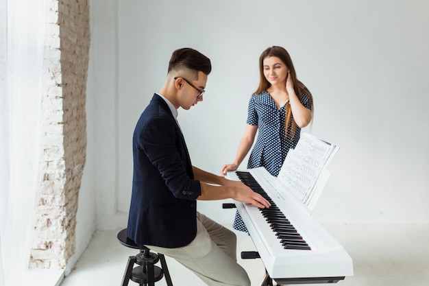 Bela jovem olhando homem tocando piano contra a parede