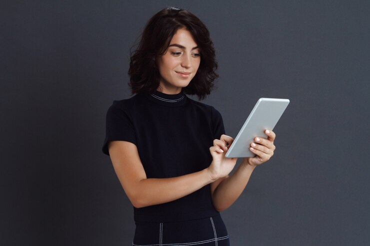 Foto grátis bela jovem posando sobre parede cinza e segurando o tablet nas mãos