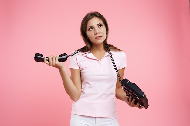 Bela jovem segurando o telefone fixo com fio de telefone em volta do pescoço