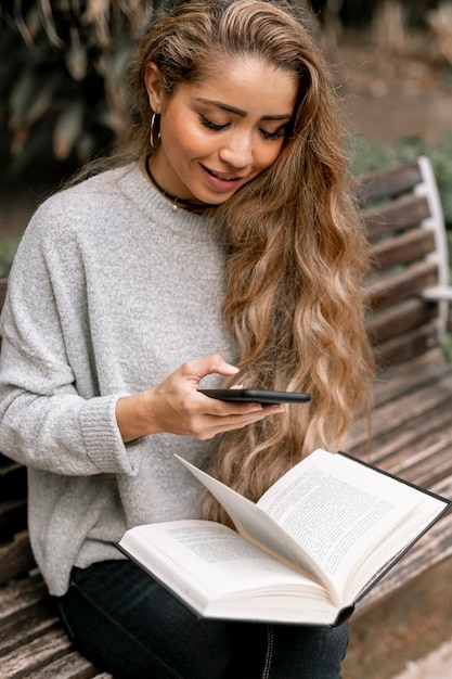 Bela jovem segurando um livro enquanto verifica seu telefone