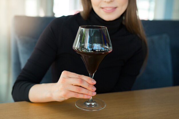 Bela jovem sentada à mesa com uma taça de vinho em um restaurante