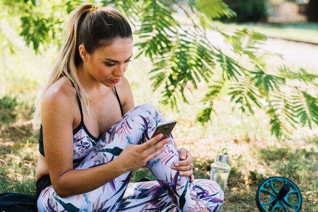 Bela jovem sentada no jardim usando smartphone