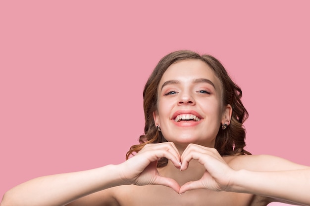 Foto grátis bela jovem sorridente com cabelo longo ondulado e sedoso, maquiagem natural com a mão perto do queixo, isolado na parede rosa.
