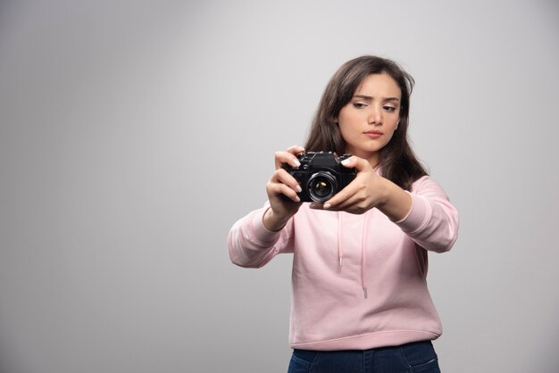 Bela jovem tirando fotos com a câmera sobre uma parede cinza.