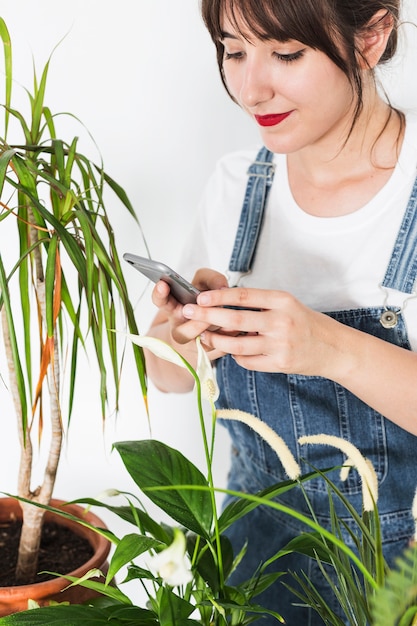 Bela jovem usando celular perto de vasos de plantas