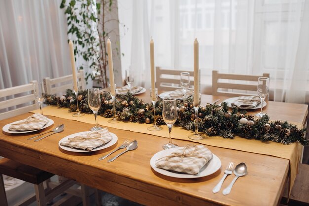 Bela mesa de servir de Natal com velas e decoração de árvore do abeto em close-up interior moderno e aconchegante. Comemorando o feriado de dezembro no ano novo cercado por copos e pratos com decoração sazonal