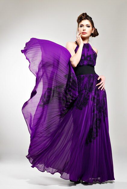 Bela moda mulher com vestido longo violeta penteado com desenho de tranças, poses no estúdio