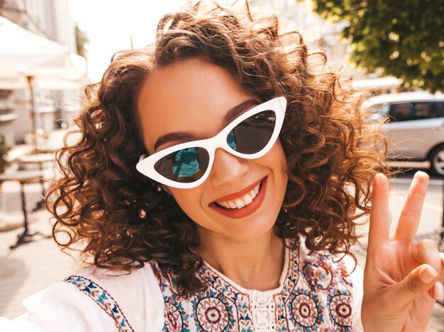 Bela modelo sorridente com afro cachos penteado vestido com vestido branco hipster de verão.