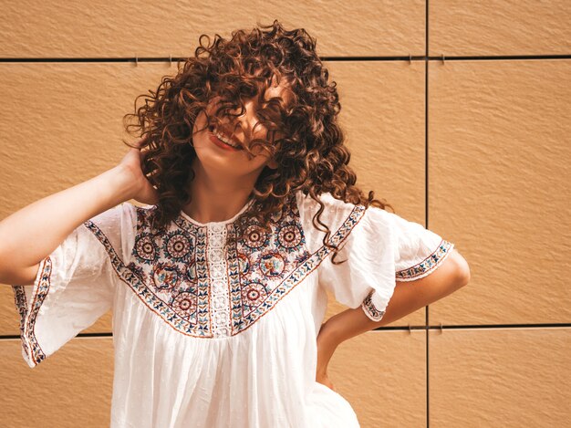 Bela modelo sorridente com afro cachos penteado vestido com vestido branco hipster de verão.