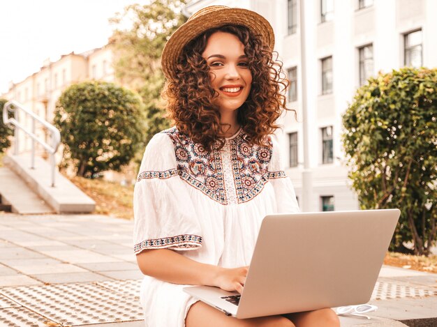 Bela modelo sorridente com afro cachos penteado vestido com vestido branco hipster de verão.