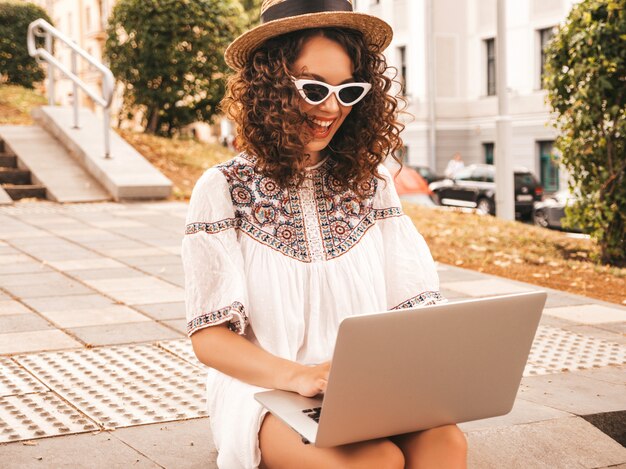 Bela modelo sorridente com afro cachos penteado vestido com vestido branco hipster de verão.